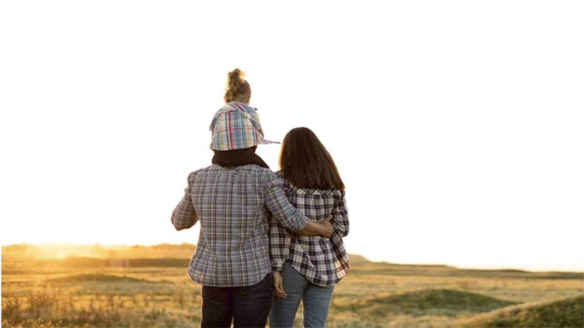A picture of the backs of a couple with a little girl on her dad's shoulders walking in the grass